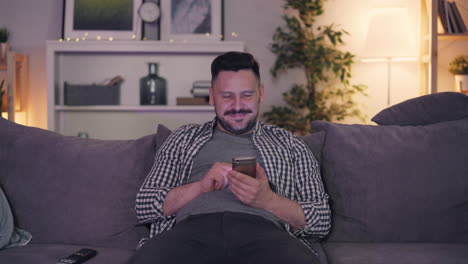man using smartphone on a couch at home in the evening