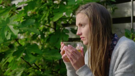 girl with long hair sits outside enjoying tea and staring out, medium