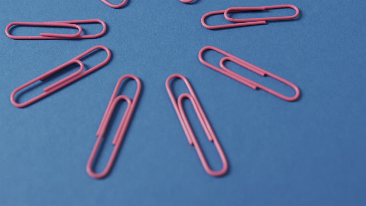 Close up of pink paper clips arranged on blue background, in slow motion
