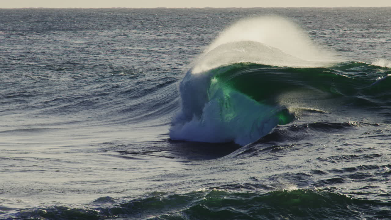 Slow motion capture of rising wave in side profile, white crest and rippling deep ocean below
