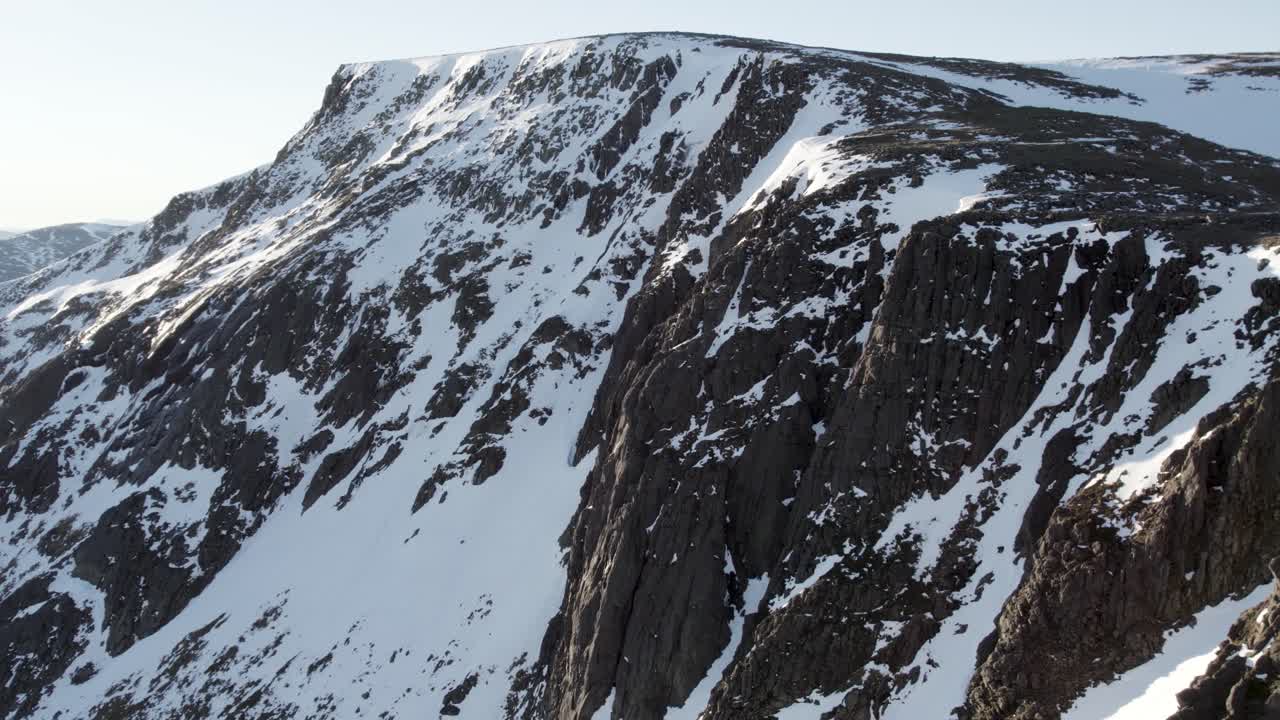 imágenes aéreas de drones que se elevan e inclinan para revelar un acantilado de montaña y barrancos llenos de nieve cerca de ben macdui en el parque nacional de cairngorms, escocia mientras el sol se refleja en la nieve en una cresta