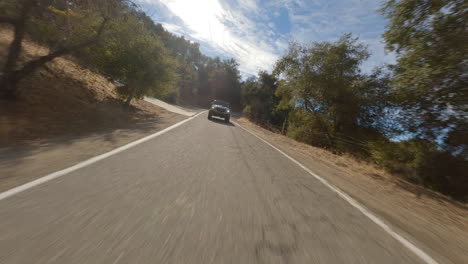 fpv drone shot of black car driving fast on road