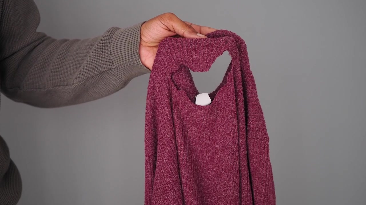 Persona che tiene un maglione lavorato a maglia color bordeaux con un buco