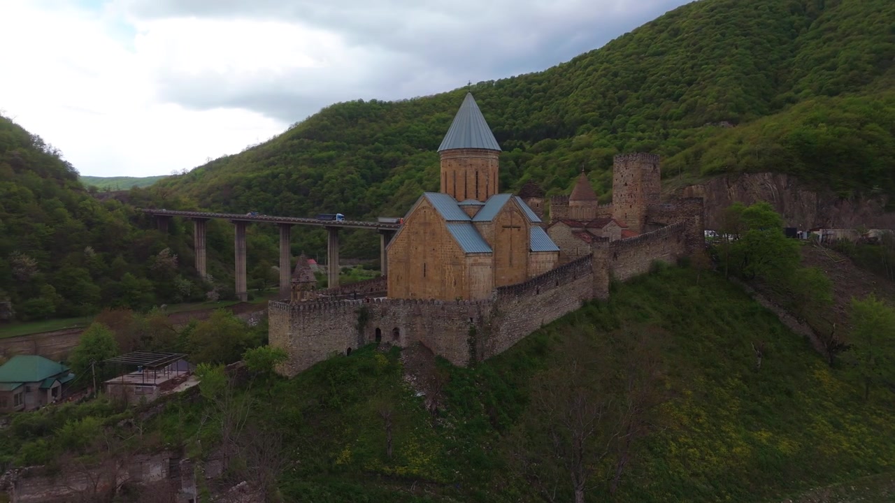 Vista aerea del complesso della Fortezza di Ananuri in Georgia, che presenta la chiesa in pietra e le fortificazioni del XVII secolo, situata su una collina accanto a un ponte moderno e rigogliose montagne verdi