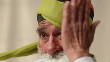 fotografía de estudio de cerca de un anciano sikh con barba atando tela para un turbante contra un fondo plano 1