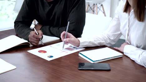 closeup of two unrecognizable business partners or economics students discussing document with graphs and charts, notepads and smartphone on table