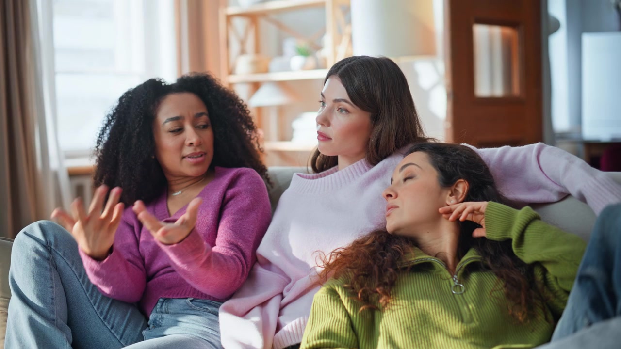 Friendly girls discussing news sitting couch closeup. Mixed-race friends talking