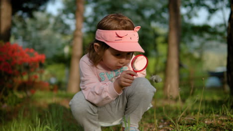 Young-girl-bending-down,-looking-at-dandelion-in-seed-through-magnifying-glass