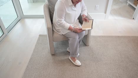 mujer lee un libro mientras está sentada en una silla, ella mira hacia arriba, sonriendo y da la aprobación de pulgares hacia arriba