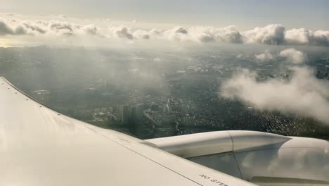 Point-of-view-of-seated-passenger-inside-air-airplane-craft-next-to-wing-motor-turbine-closeup-with-wings-and-city-background-in-sunrise-skyline