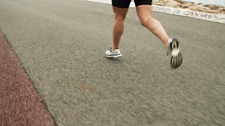 Gambe di un'atleta donna che fa jogging lungo una strada costiera