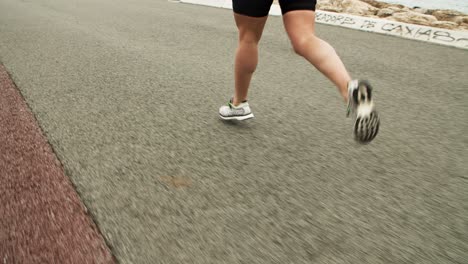 legs of female athlete jogging along seaside road