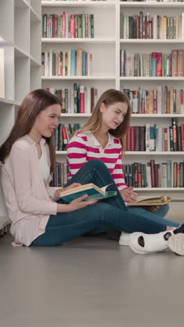 happy friends sit on floor discussing startup project in public library. women and black man read books together in bookstore. students group do homework together