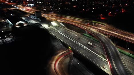 Drohnenaufnahme-Des-Nächtlichen-Verkehrs-Auf-Einer-Autobahn-Mit-Autos-Und-Lichtspuren-Mit-Tunnel-Und-Viadukten-Außerhalb-Der-Stadt-Warschau,-Polen