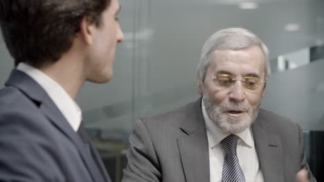 mature businessman talking to younger colleague