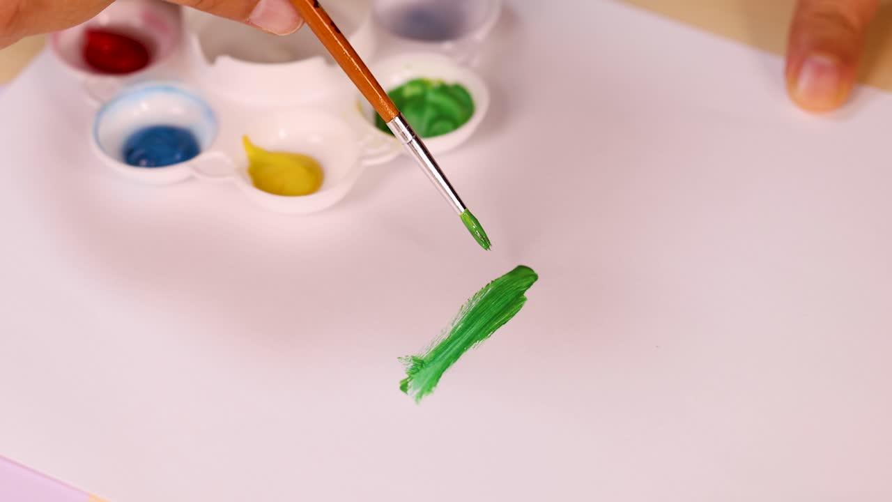 Artist hand paints green watercolor stroke on paper, bright lighting, overhead view, steady camera