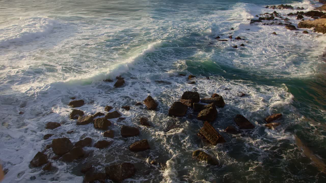Tilting up on blue ocean with waves crashing on rocks in Syracuse, Sicily (Sicilia, Italia)