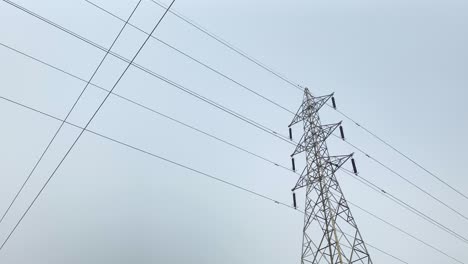 una toma en ángulo bajo de una torre eléctrica de alto voltaje contra un cielo azul, que representa el poder y la infraestructura de la sociedad moderna