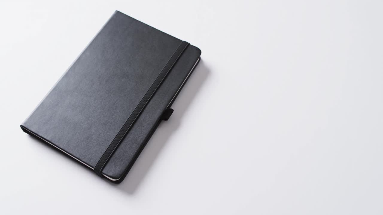 Close up of closed black notebook with copy space on white background in slow motion