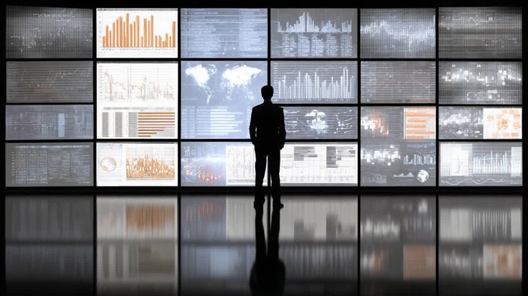 A contemplative figure stands before a vast array of data visualizations, immersed in analysis within a high-tech environment that reflects modern data interpretation