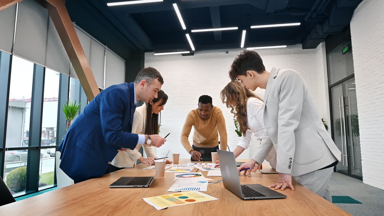 Grupo multirracial de personas en una reunión de negocios en una oficina, debatiendo asuntos empresariales entre ellos con papeles y dispositivos sobre la mesa