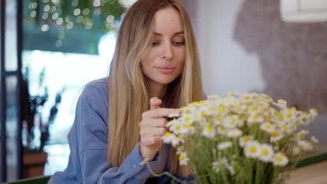 blonde woman looking and touching beautiful bouquet of chamomile flowers