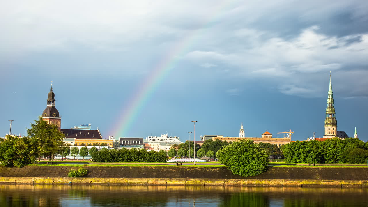 toma de lapso de tiempo del hermoso arco iris sobre la ciudad de riga durante un día nublado, letonia - hermosas iglesias, río daugava y autos en la carretera