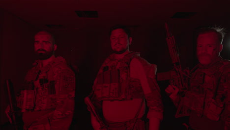 front view of soldiers in bulletproof vests standing in dark room and looking at camera