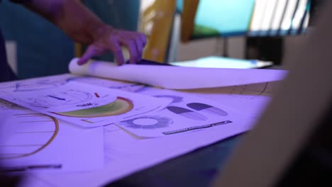 man rolling out his design papers or blueprints on his desk in his studio with view of his hands and arms only as he is surrounded by work equipment