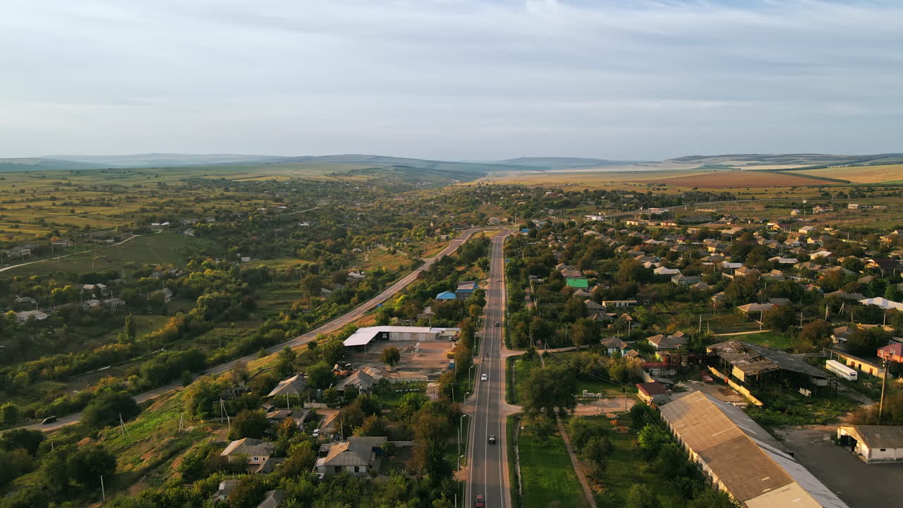 Aerial drone view of village in Moldova. Residential buildings, greenery, road with moving cars, wide fields