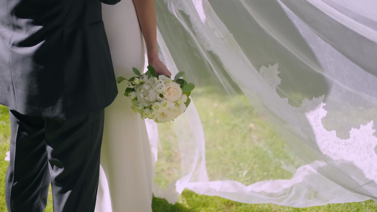 wedding couple standing close with flowers and veil in sunlight