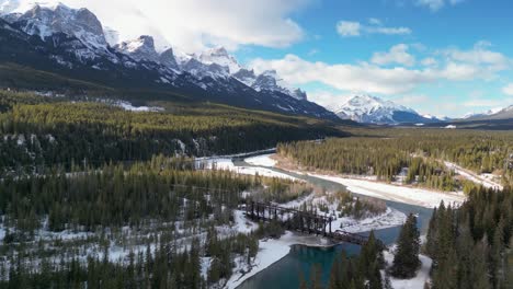 Aerial-of-river-with-bridge-and-mounatins-in-background,-Bow-River,-Alberta,-Canada