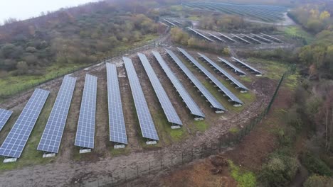 Solar-panel-array-rows-aerial-view-misty-autumn-woodland-countryside-orbit-low-left