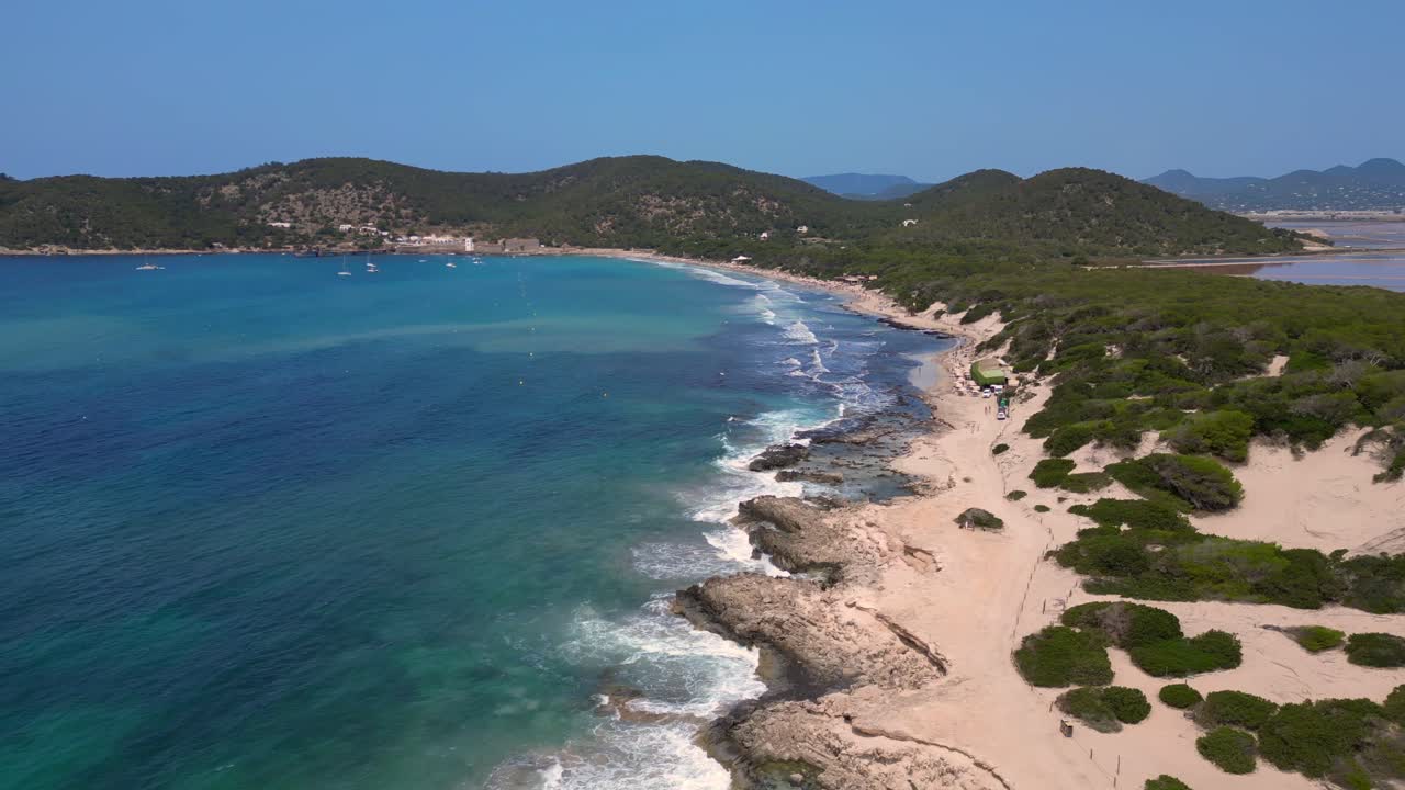 Turquoise waves crashing on the rocky coast of Ses Salines beach with the ancient watchtower. Marvelous aerial view flight overflight flyover drone