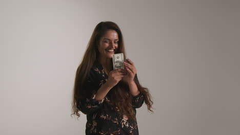 studio shot of excited woman celebrating winning cash prize throwing handful of 100 dollar bills in the air