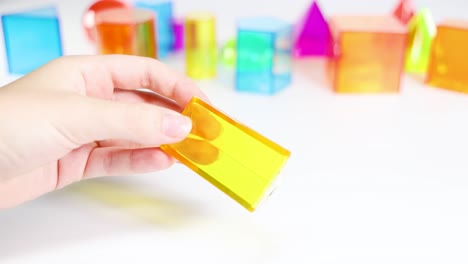 hands manipulate vibrant 3d shapes on a white surface, highlighting geometry and color in a bright, educational setting