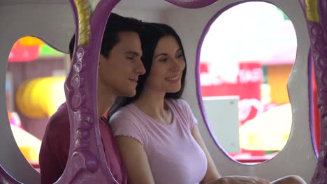 couple in love sitting on pumpkin carriage in carousel holding hand together at the amusement park outdoors in summer having fun in vacation