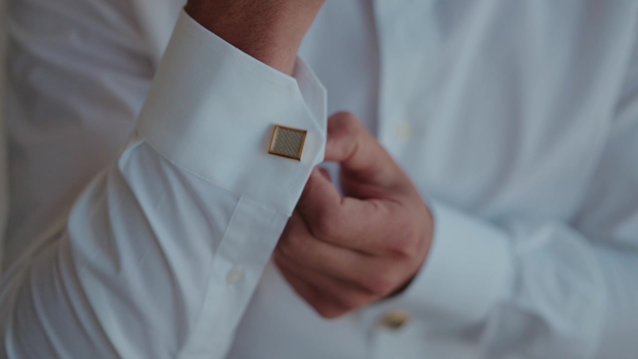 Una mano sistema un gemello d'oro sul colletto di una camicia bianca immacolata durante la preparazione di un abito formale