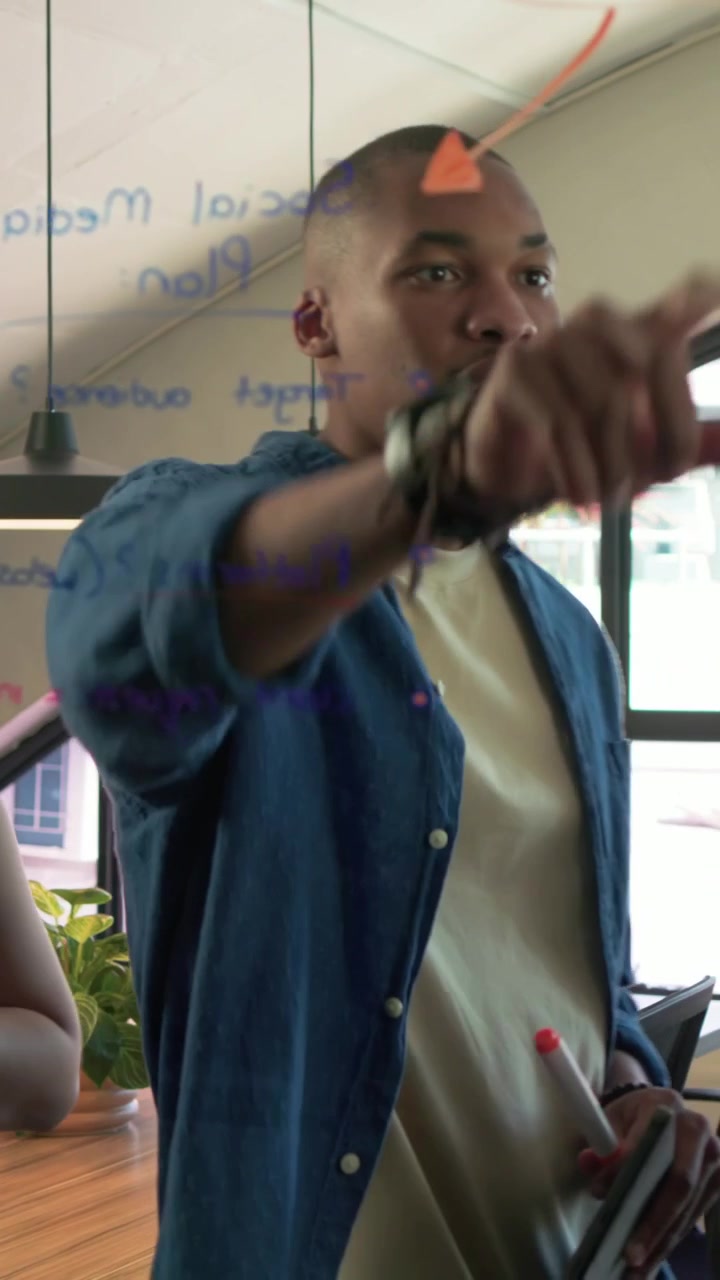 Vertical video: Seeing pink marker writing blue-shirt man adding notes on glass meeting for revenue