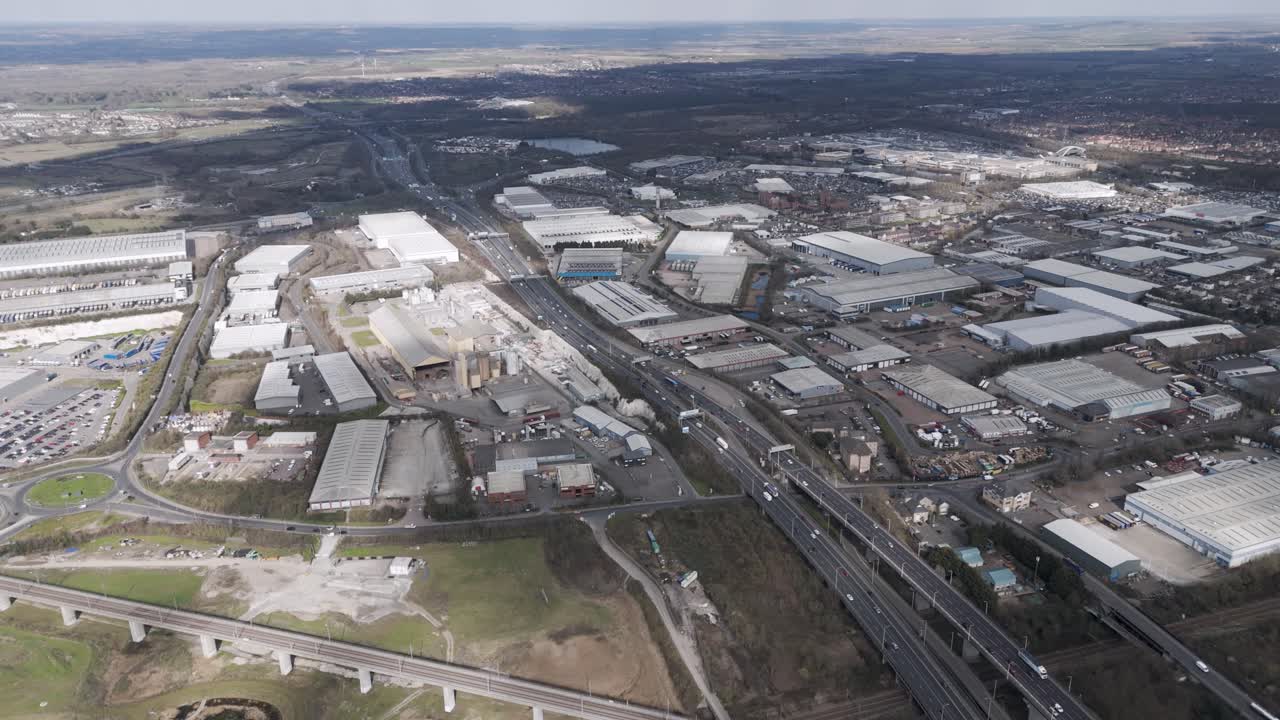 Aerial tracking shot of multilayer A282 interchange with sparse traffic, elevated flyovers and warehouse roofs framing industrial landscape, Thurrock, Essex, UK, March 2025