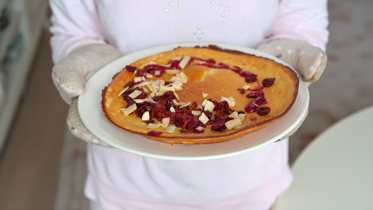 Hands holding a pancake with dried fruits an nuts on a white plate