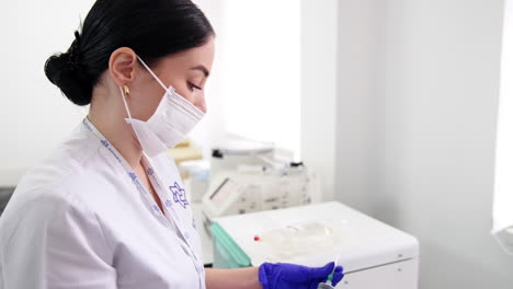 dark-haired female medic in white robe and mask prepares a syringe. getting ready for taking blood samples.
