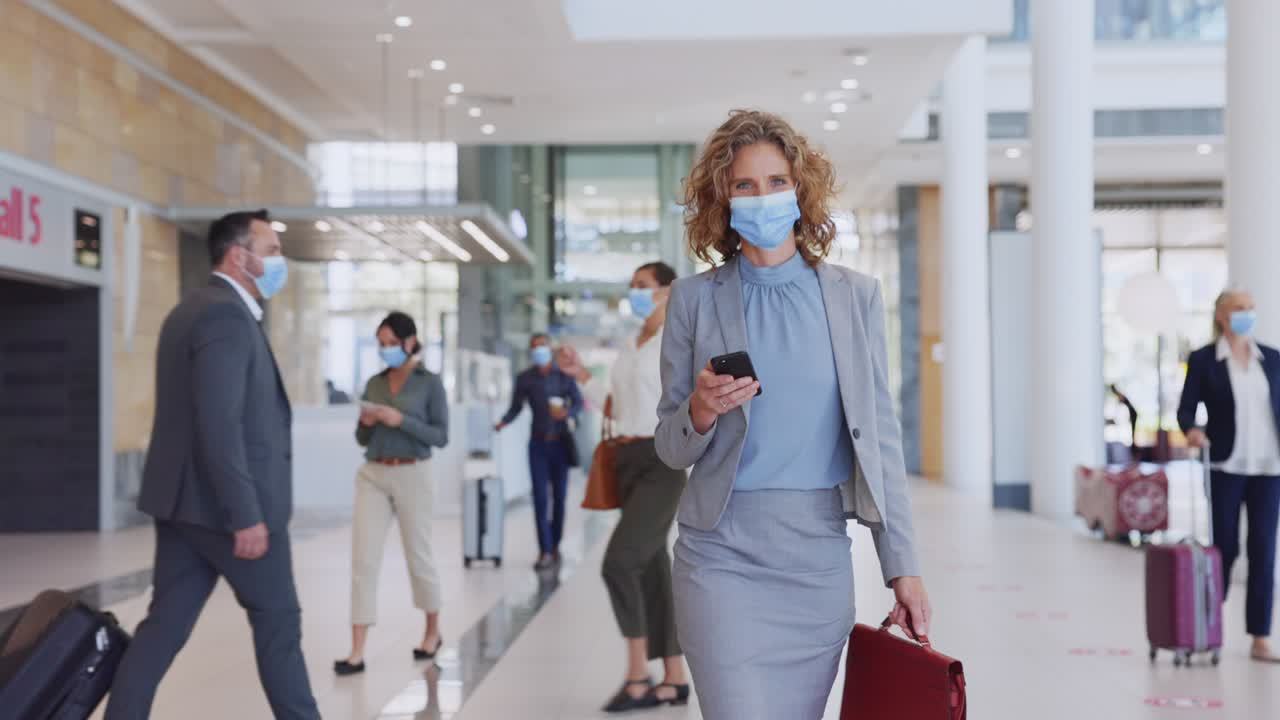 Pengusaha wanita mengenakan masker wajah dan memeriksa ponselnya di bandara.