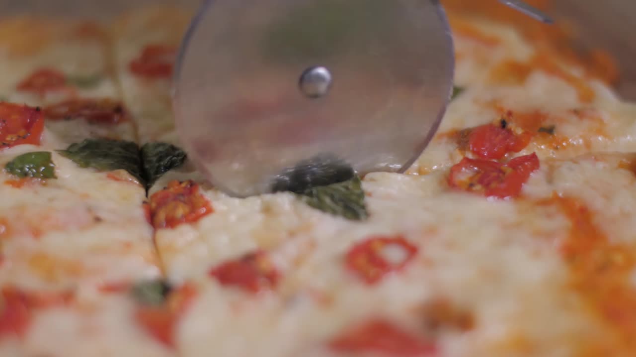 A pizza cutter slicing through a fresh pizza on a wooden chopping board