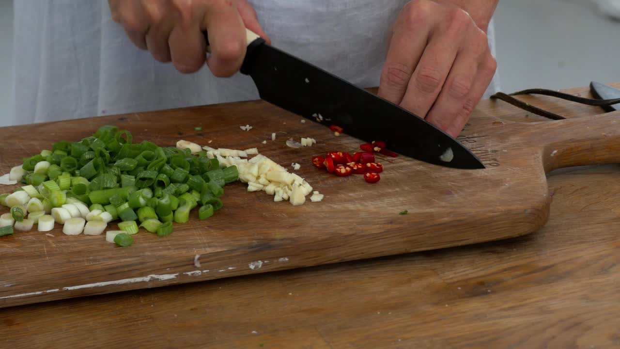 Slicing fresh hot chillies on a board among celery and garlic in preparation to cook
