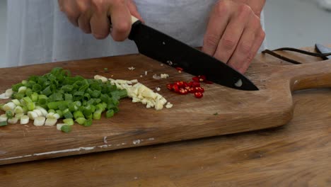 slicing fresh hot chillies on a board among celery and garlic in preparation to cook