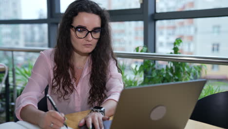 business lady works with laptop at the table. working on computer and taking notes. woman concentrated on her work.