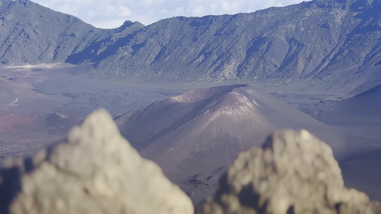 Cinematic shot with foreground elements of the volcanic cinder cone craters at the summit of Haleakala in Maui, Hawai'i