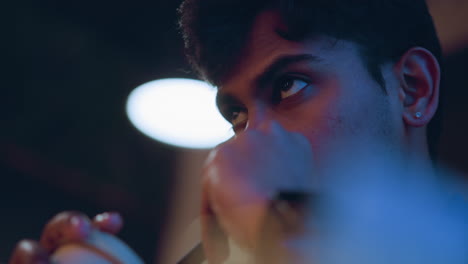 close-up of young man drinking from takeaway cup through black straw with intense focused gaze, wearing smart shirt and wristwatch, warm ambient lighting and soft blur in background create contemplative atmosphere