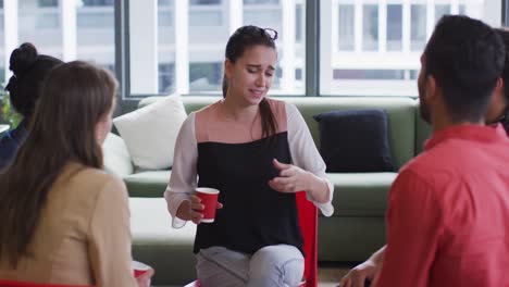 Caucasian-businesswoman-holding-red-cup-in-a-meeting-with-diverse-group-of-colleagues